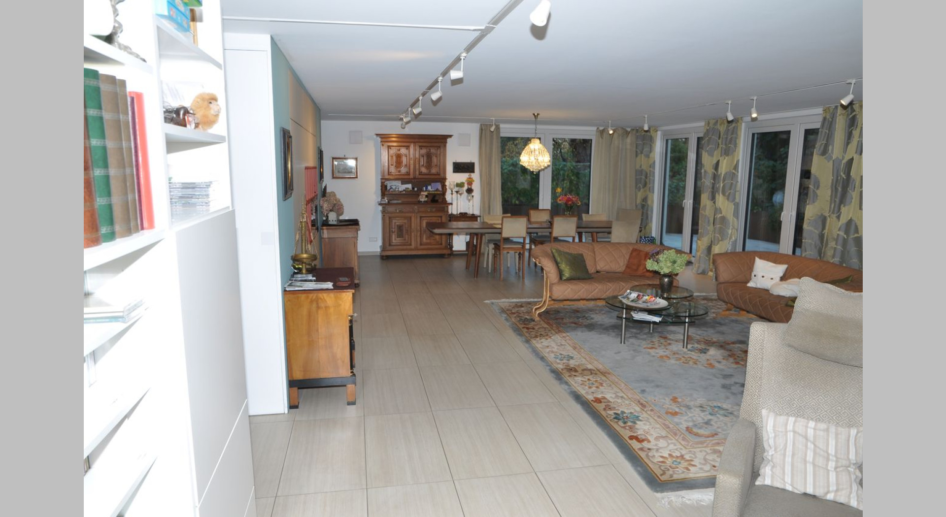 Das Wohnzimmer mit großem Esstisch, Sitzecke mit 2 kleinen Ledersofas, Fernsehecke und Bücherregal ist sehr geräumig und hat an 2 Seiten mehrere Türen, die sich zur Terrasse öffnen.