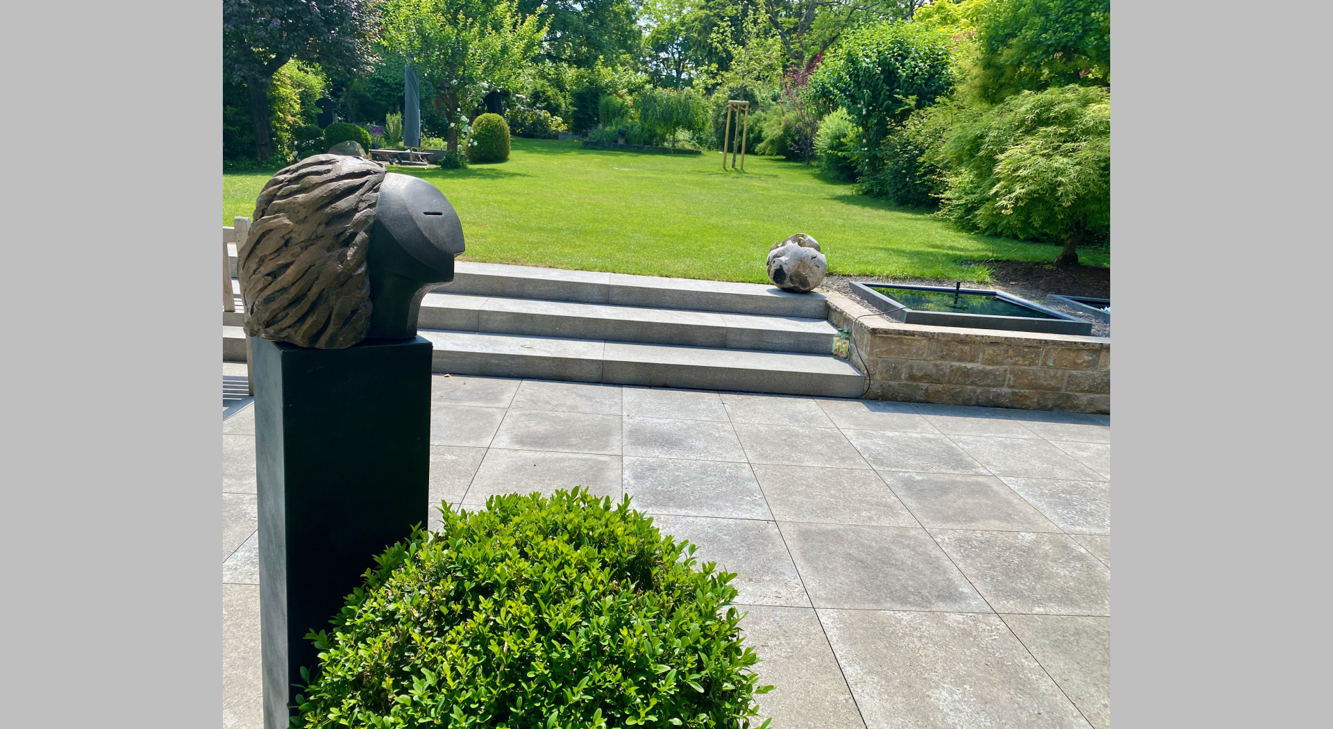 Vordergrund Skulptur, Terrassen Teilansicht und Blick in den Garten
