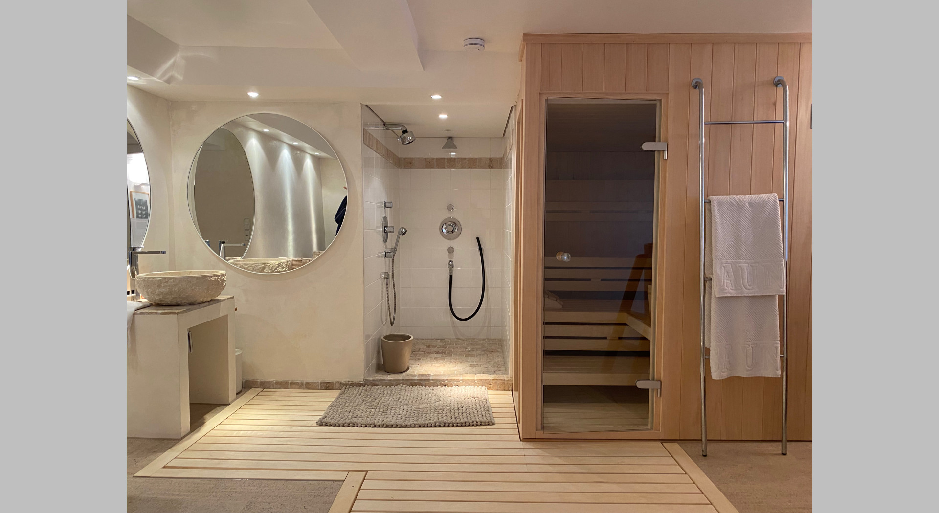 Blick auf Sauna Dusche und z:T. Waschbecken mit 2 grossen runden Spiegeln über Eck