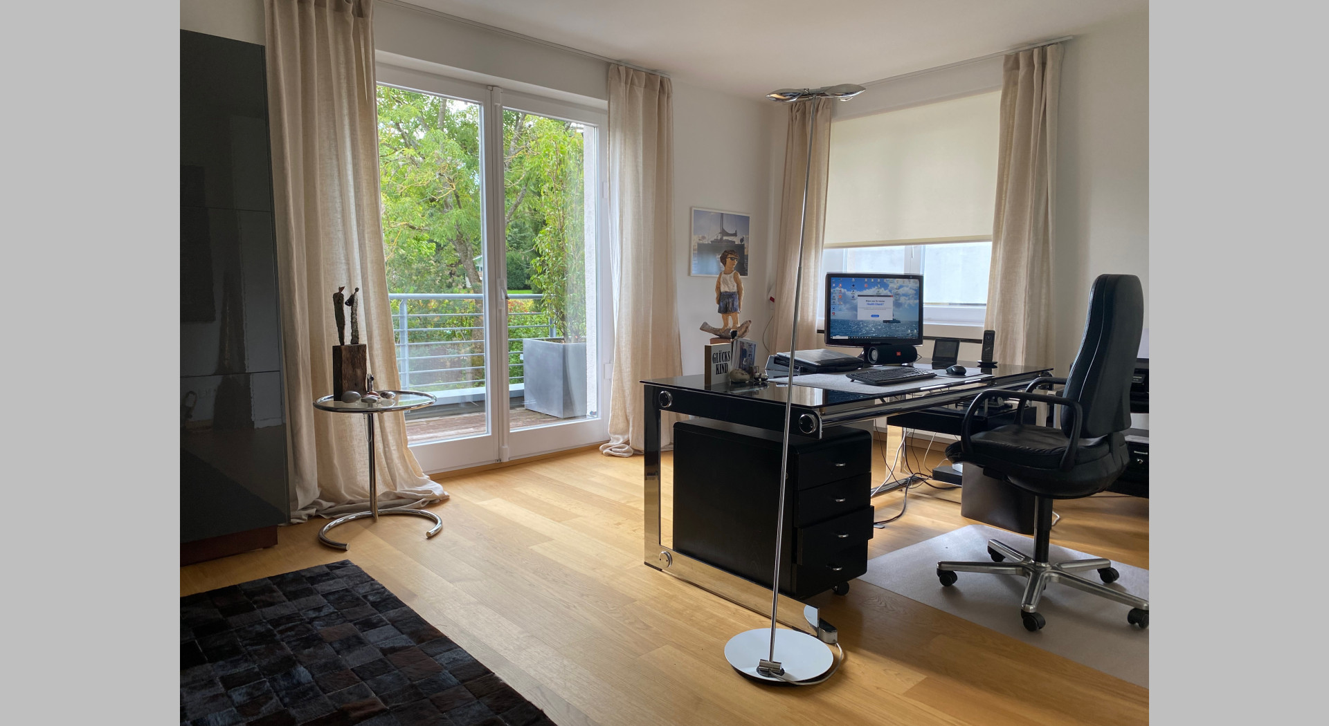 Ein Büro; Schreibtisch und Fenstertüre auf die Dachterrasse und Blick in den Garten