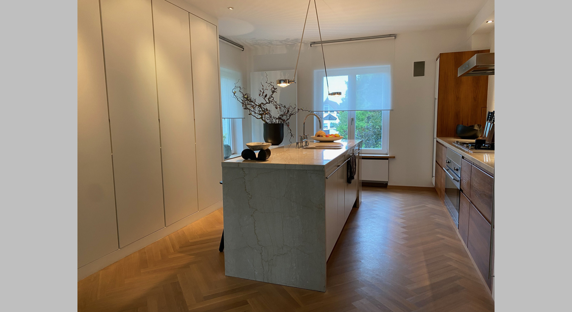 Steinerner Küchenblock in der Mitte der Küche, Deckenhohe Schränke links, zwei Fenster über Eck hinten